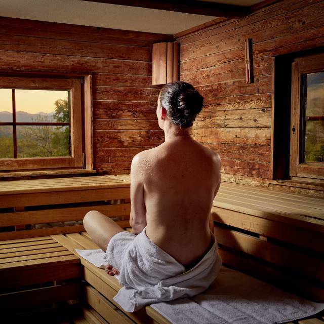 Frau von hinten sitzt in Sauna mit Blick auf die Berge